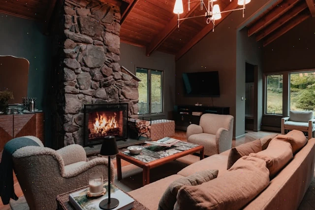 Cozy living room with a stone fireplace, sofa, armchairs and a chandelier under a wooden ceiling